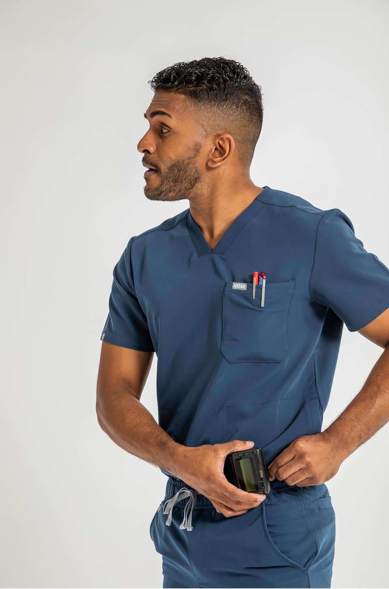 VENA mens jogger style scrub shirts man putting the beeper on his side waist#colour_navy-blue