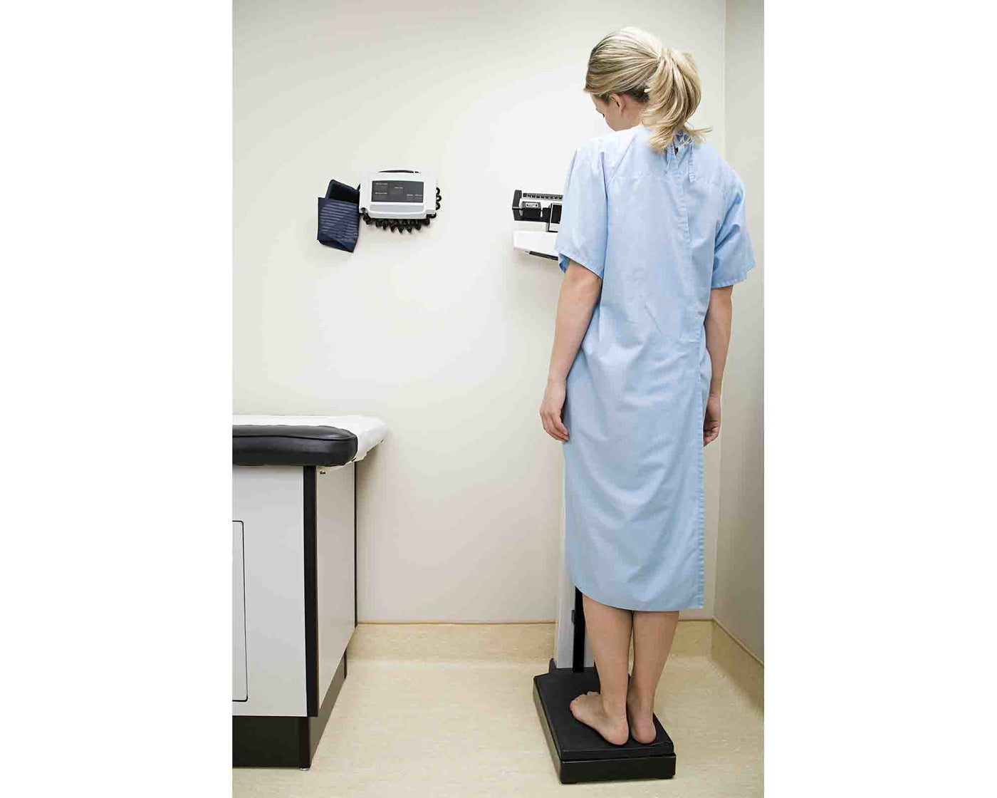 A woman weighing herself and wearing light blue hospital patient gown